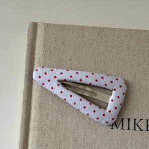 Detailed close-up of a white fabric hair clip with red polka dots on a book cover