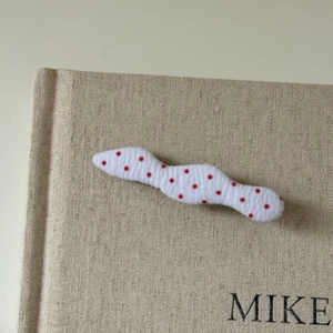 Detail view of wavy white fabric hair clip with red polka dots on linen book cover