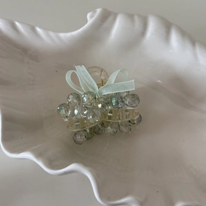 Close-up of a blue crystal beaded hair claw clip with a green chiffon bow on a white tray