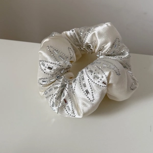 Détail macro du chouchou en satin crème avec broderie de perles argentées et strass