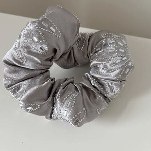 Détail d'un chouchou en satin gris avec broderies complexes de strass et de perles fines