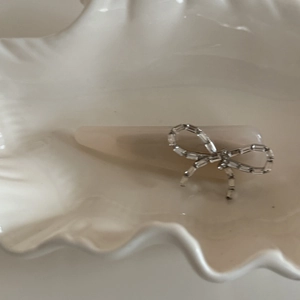 Elegant off-white acrylic bow hair clip with sparkling silver zircon stones on a shell plate
