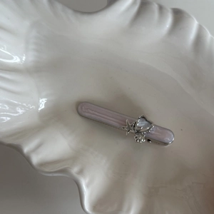 Detail of pink pearlescent starfish hair clip with silver shells on white shell plate