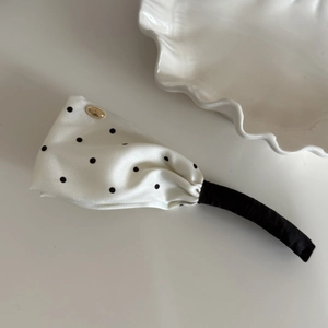 Detailed view of white satin polka dot hair clip with elegant gold oval metal emblem