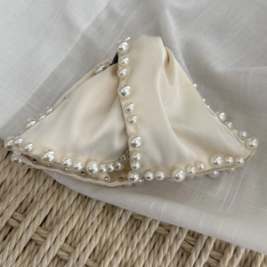 Détail d'une pince à cheveux chic blanc cassé avec bords en perles et texture soie