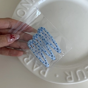Close-up of blue polka dot BB hair clips set held in hand over a white ceramic plate