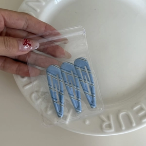 Close-up of three blue and white striped teardrop hair clips in a simple plastic bag