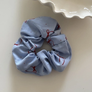 Detail eines hellblauen Haargummis mit roten Schleifenmustern und Punkten auf weißem Tisch