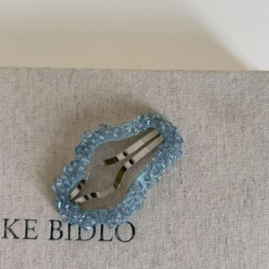 Détail macro d'une barrette BB argentée avec cristaux bleu clair sur un fond de tissu texturé