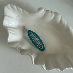 Détail d'une barrette ovale cyan avec strass et texte Creation France sur plat coquille
