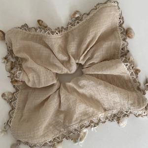 Detail of beige linen hair scrunchie with lace trim, shell and starfish charms