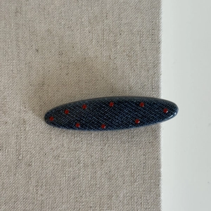 Polka dot denim blue oval hair clip with red spots for women on beige fabric background