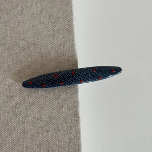 Detail view of denim blue hair clip with red polka dots on a minimalist split background