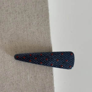 Detailed macro view of a denim texture hair clip with red polka dots on white and linen