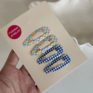 Detail view of 4-piece plaid snap hair clip set on beige display card for girls