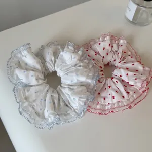 Blue and red polka dot scrunchies with floral embroidery and lace trim on white surface