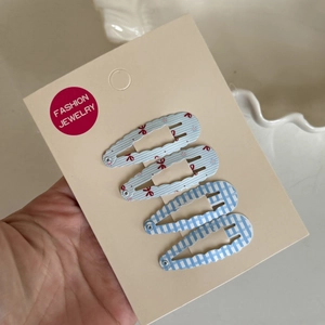 Detail showing set of four blue hair clips with bow, dot and plaid patterns on card