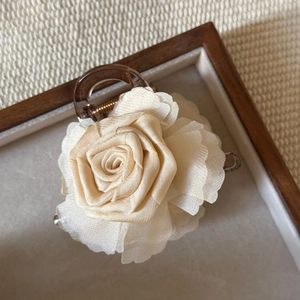 Detail view of a cream fabric rose hair claw clip on a rustic wooden tray texture