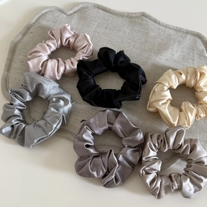 Detailed view of six silk satin scrunchies in pastel pink, black, and gray tones