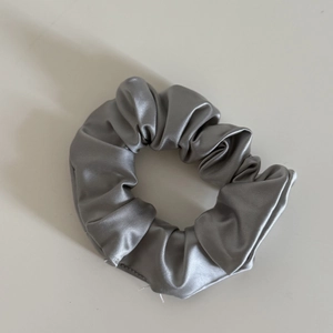 Silver satin hair scrunchie with pleated elastic design and metallic glossy finish