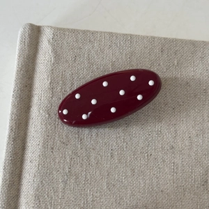 Retro dark red oval hair clip with white polka dots on beige fabric background
