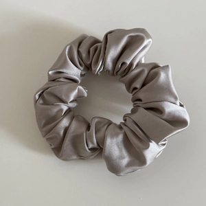 Close-up of champagne silk satin hair scrunchie showing pleated texture and glossy finish