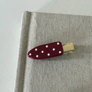 Retro cherry red duckbill hair clip with white polka dots on textured background