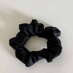 Detailed view of black satin pleated scrunchie with smooth texture and glossy finish