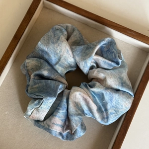 Detailaufnahme des blau-marmorierten Haargummis mit Satintextur auf einem Holztablett