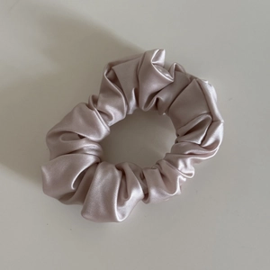 Detailed view of the soft champagne pink satin silk scrunchie with glossy pleated texture