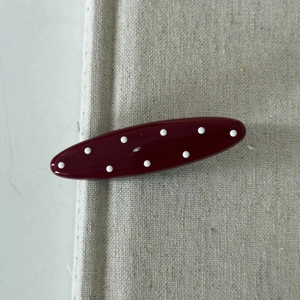 Close-up of a burgundy red polka dot hair clip on a textured fabric background