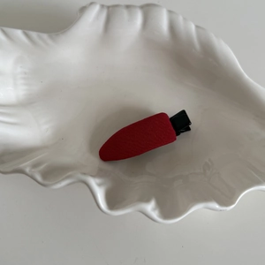Détail d'une pince à cheveux en tissu rouge vif sur un plateau en céramique blanc