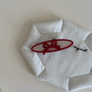 Detailed view of red and white acetate hair clip with a delicate bow on a white coaster