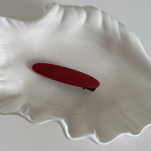 Gros plan sur une barrette en tissu rouge texturé posée sur un plateau en forme de coquille