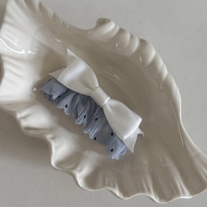 Macro detail of white lace bow hair clip with black polka dots on a shell plate
