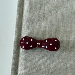 Macro view of cherry red polka dot resin bow hair clip on a textured fabric