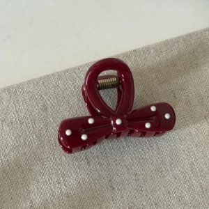 Detail view of a cherry red polka dot bow hair claw clip on grey textured fabric