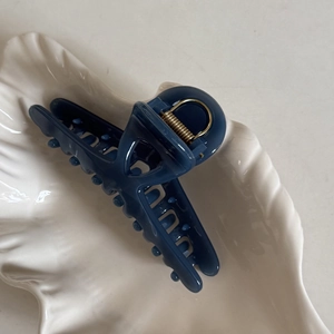 Détail d'une pince à cheveux mate bleu marine avec ressort en métal doré sur plateau