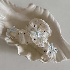 Detailed view of white polka dot lace scrunchie with blue bow and pearl in shell tray