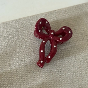 Detail view of a cherry red polka dot bow hair clip on a textured beige background