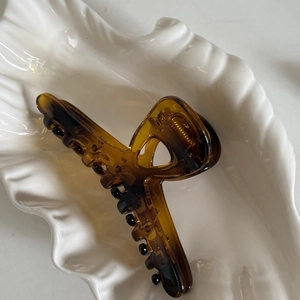 Détail d'une grande pince à cheveux en résine ambrée avec ressort en métal doré sur plat