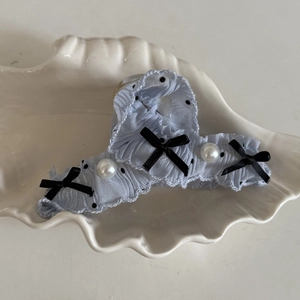 Close-up of light blue polka dot hair claw clip with black bow and pearl detail