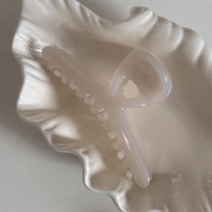 Détail d'une grande pince à cheveux blanc crème au fini perlé sur un plateau en céramique