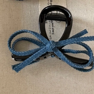 Detail of blue denim bow on black hair claw clip with cream fabric background