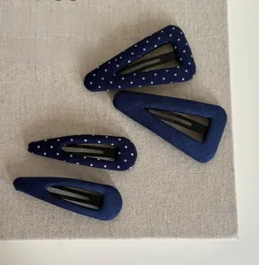 Close-up of navy blue and polka dot fabric hair clips on beige linen texture surface
