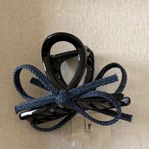 Detailed close-up of a denim bow hair claw clip with its original tag on beige fabric