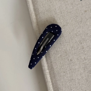 Navy blue polka dot drop-shaped BB hair clip on a minimalist fabric book background