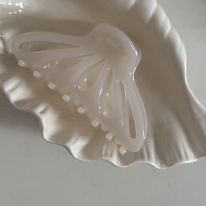 Macro di una molletta per capelli traforata bianco crema su un vassoio di ceramica