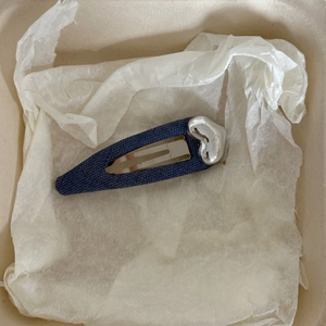 Dettaglio di un fermaglio per capelli in denim blu con un ciondolo a forma di cuore argento