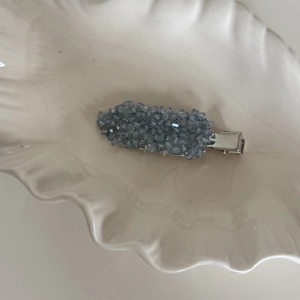 Elegant silver hair clip with sparkling blue crystals and stones in a white shell tray